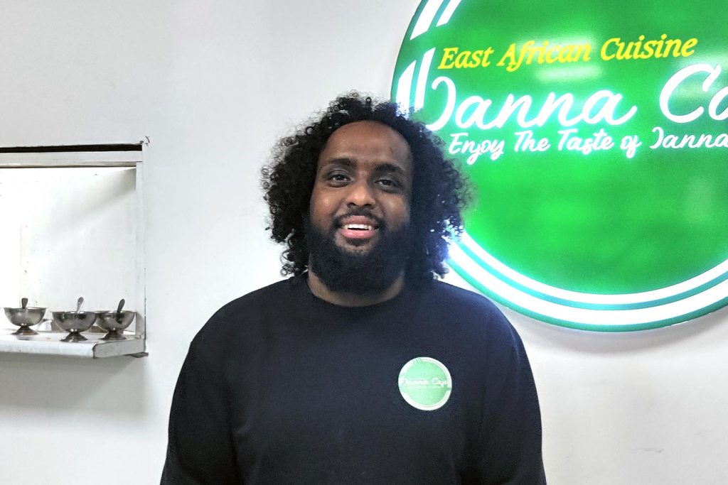 Owner Musa standing by the sign in Somali food restaurant Janna Cafe in Whitechapel, East London.