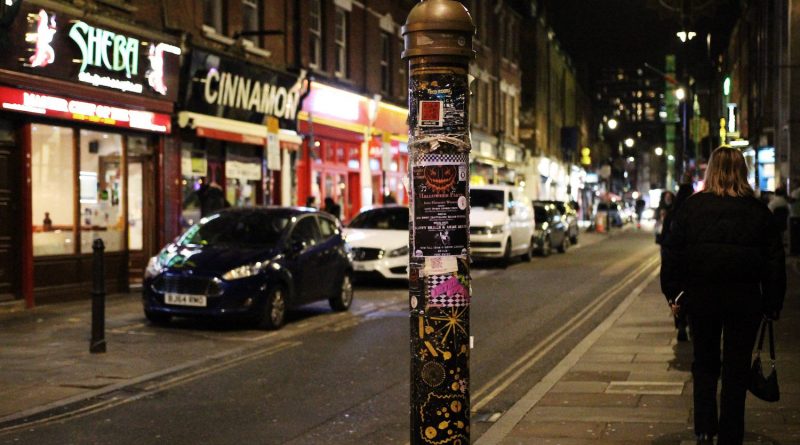 The Banglatown decorated lamp post in focus with the curry houses blurred behind it.