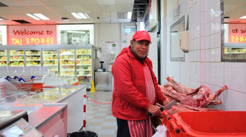 Taj Stores butcher at his work station, cutting up some meat, as he poses for the camera, Brick Lane, Whitechapel.