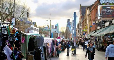 Market stalls along the pavement with the cityscape of London towering behind it, Whitechapel.
