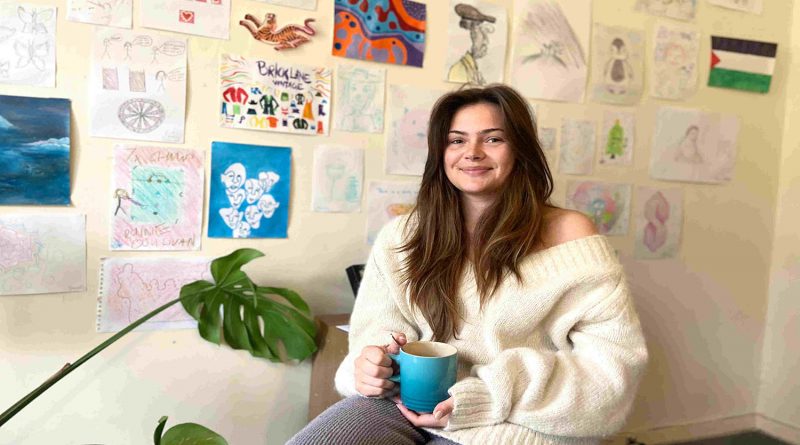 Victoria sat by her wall of art in her house in Aldgate East